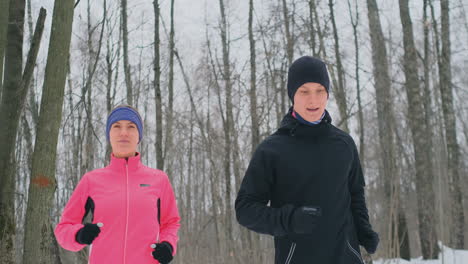 Un-Hombre-Y-Una-Mujer-Con-Una-Chaqueta-Rosa-En-Invierno-Corriendo-Por-El-Parque-En-Cámara-Lenta.-Estilo-De-Vida-Saludable