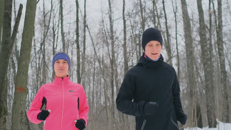 un hombre y una mujer con una chaqueta rosa en invierno corriendo por el parque en cámara lenta. estilo de vida saludable