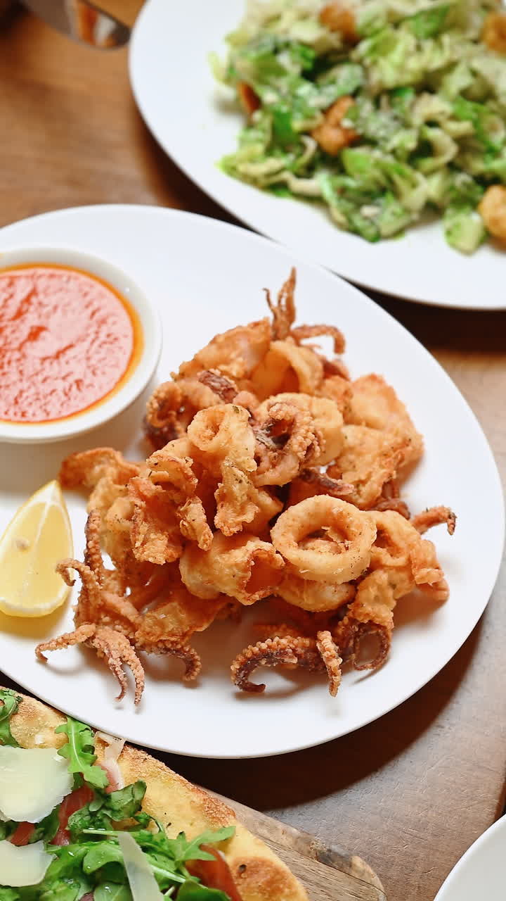 Frittura di pesce croccante servita con salsa e limone su un piatto bianco. Piatto di frittura di pesce con salsa di accompagnamento e limone a lato, gustato in un ambiente informale