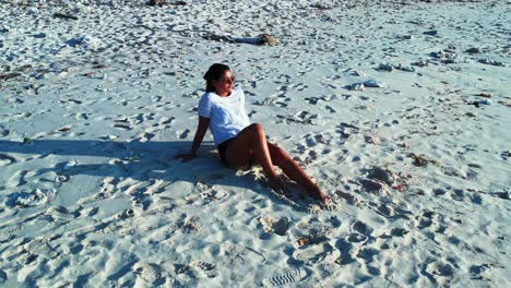 turista sentado en la playa de arena blanca de la isla de las bahamas disfrutando de la brillante luz del sol - amplio tiro rodante