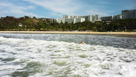 woman lying on surfboard paddling with arms towards beach