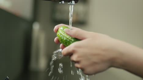 Manos-Femeninas-Lavando-Un-Pepino-Verde-Con-Agua-Corriente-De-Un-Grifo-De-Cocina