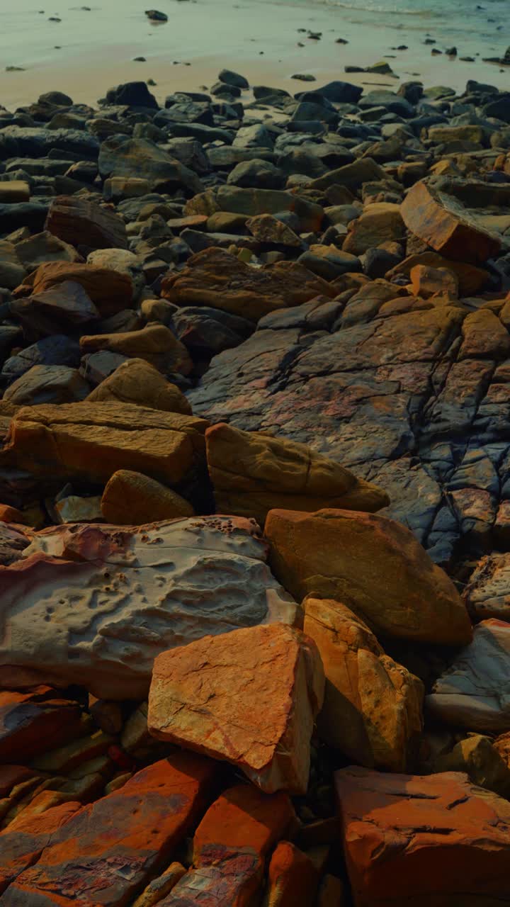 Ripresa verticale che mostra onde che si avvicinano alla riva di una spiaggia con rocce in primo piano a Langkawi, Malesia