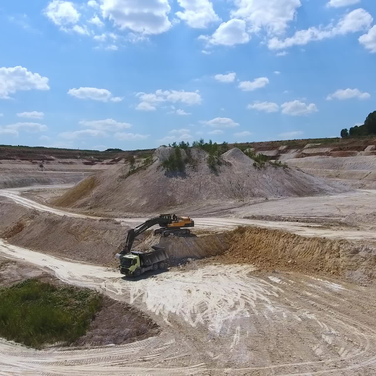 Mining the clay mineral at kaolin quarry. Excavator uploading industrial minerals into the truck for delivering it to the factory