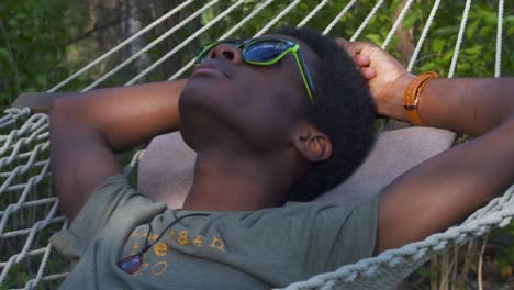 young black man resting on swinging hammock outdoors hands behind his head