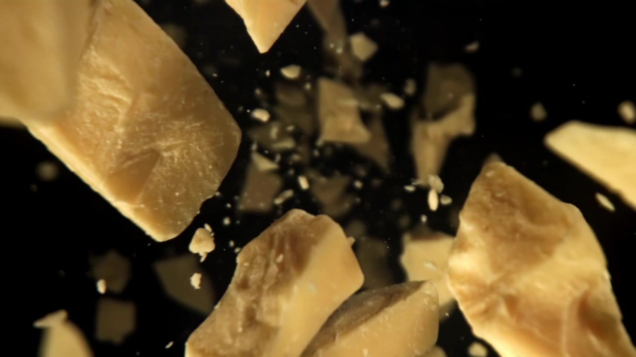 Pezzi di Parmigiano Reggiano che cadono al rallentatore su sfondo nero