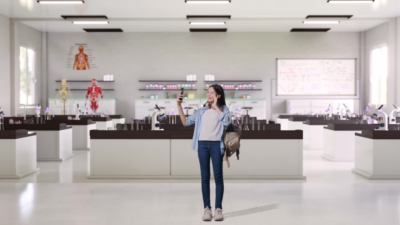 과학 실험실에 서 있는 동안 스마트폰으로 비디오 통화를 하는 배과 몇 권의 책을 가진 아시아 십대 소녀 학생의 몸이 가득 차 있습니다.