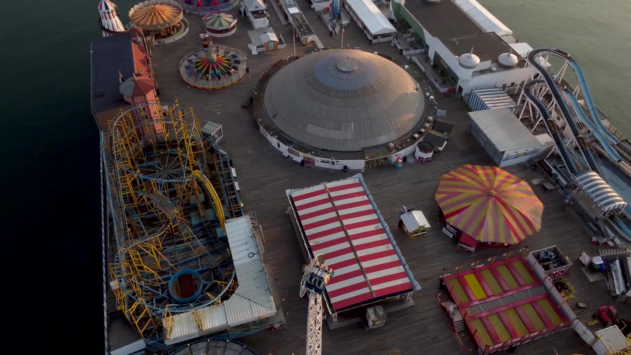 Drone shot looking down onto rides and a fun fair on a pier out to sea as the sun rises