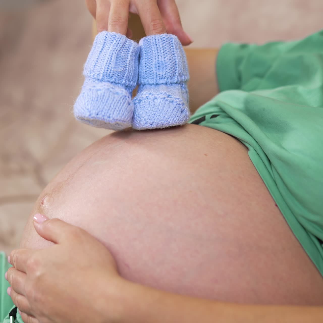 Primo piano di una donna incinta che tiene in mano delle scarpine da neonato a casa. Donna incinta di otto mesi con delle scarpine blu sul ventre.