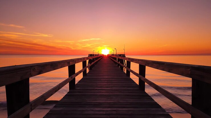 Wooden pier stretching towards a vibrant orange sunset over ocean