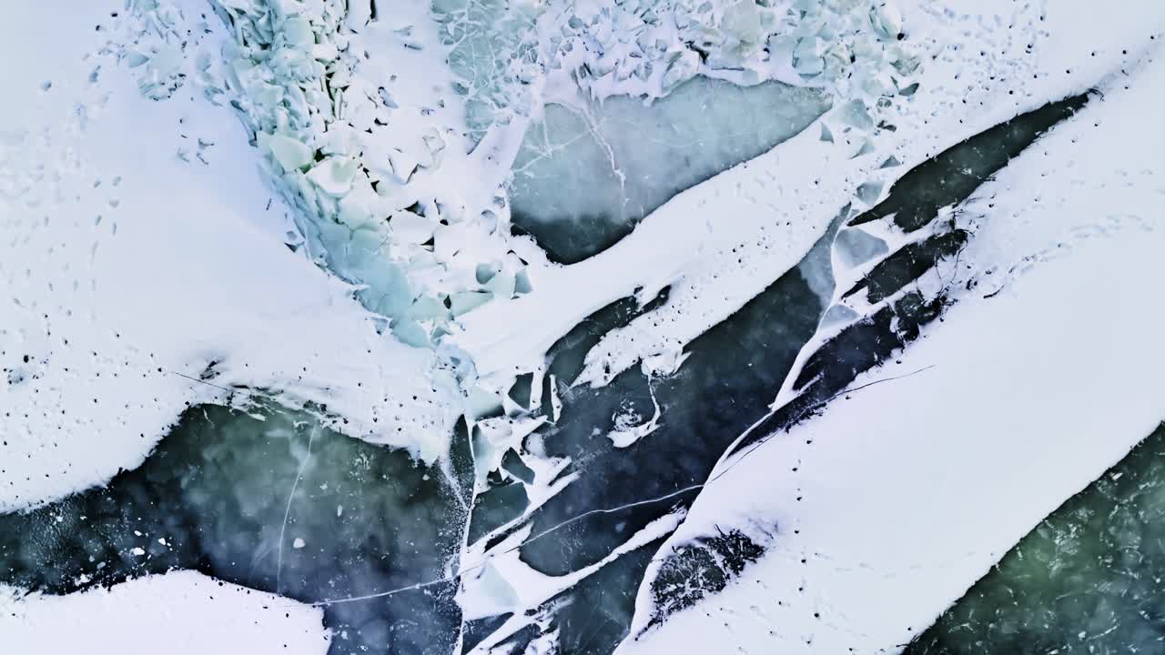 寒い沿岸の風景の中、雪の筋、暗い水の隙間、そして印象的な抽象的な模様を伴う砕けた冬の海氷のドローンによる真上からのショット。