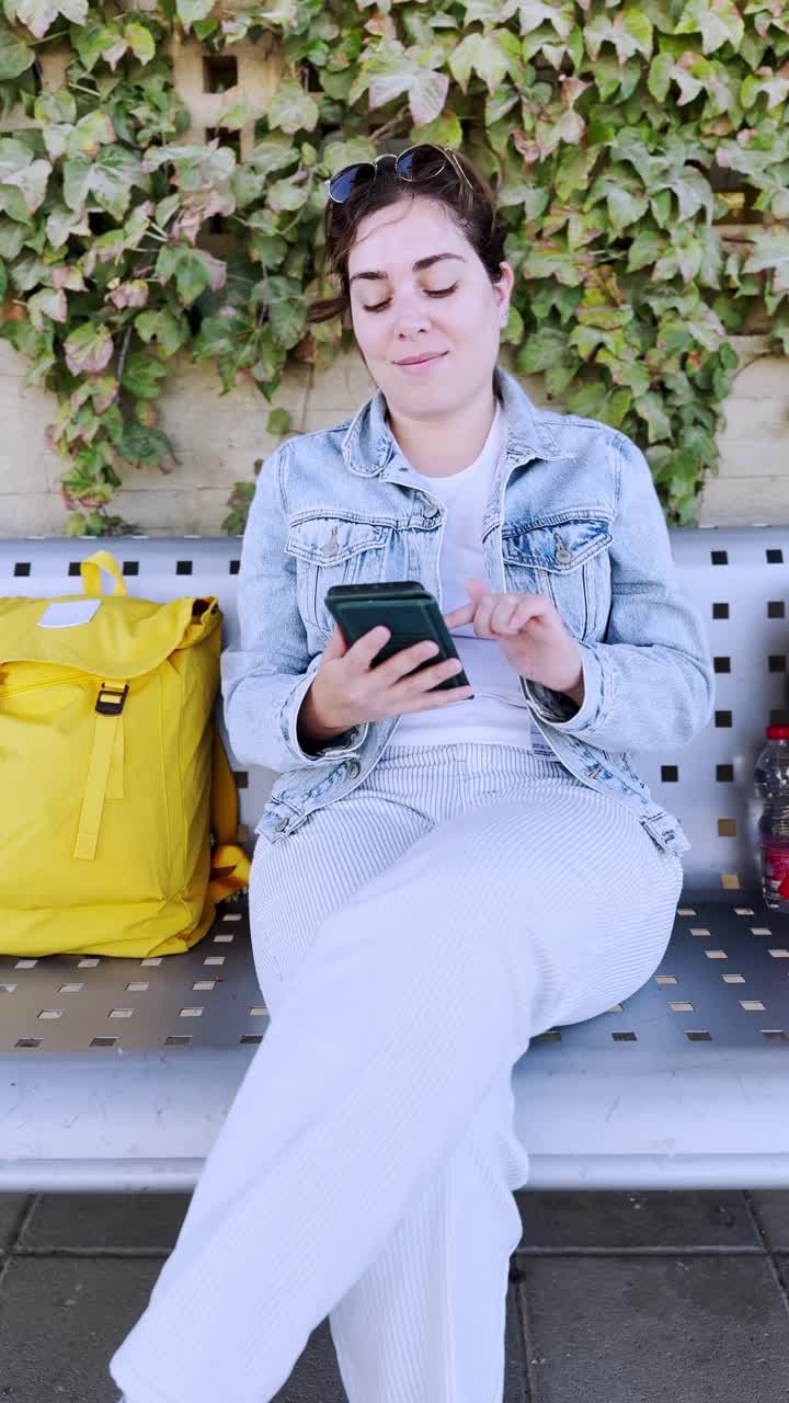 A Young Female Traveler with a Backpack Using Her Phone at a train station platform