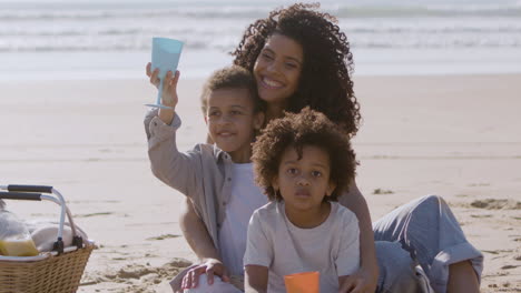 smiling black woman and two adorable children having picnic at seashore on a sunny day