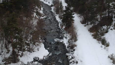 Vista-Aérea-De-Un-Pequeño-Río-En-El-Campo-Rural-En-Un-Día-De-Invierno-Nevando,-Disparo-De-Drones