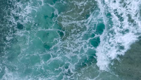 Top-Down-Slow-Motion-Drone-View-of-turquoise-clear-water-and-crashing-waves-over-shallow-coral-reef-in-Uluwatu-Bali-Indonesia