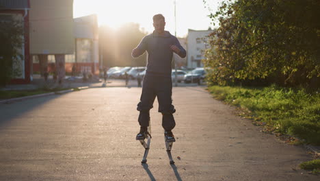 chap jumping on stilts wearing gray hoodie and dark gray pants during sunset in residential area surrounded by houses, trees, and people, showcasing urban energy, balance, and dynamic motion