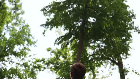 Father throwing son in air, slow motion. Father and son having fun in a green park, father throwing young boy up into the air. Happy little cute boy. Backside view
