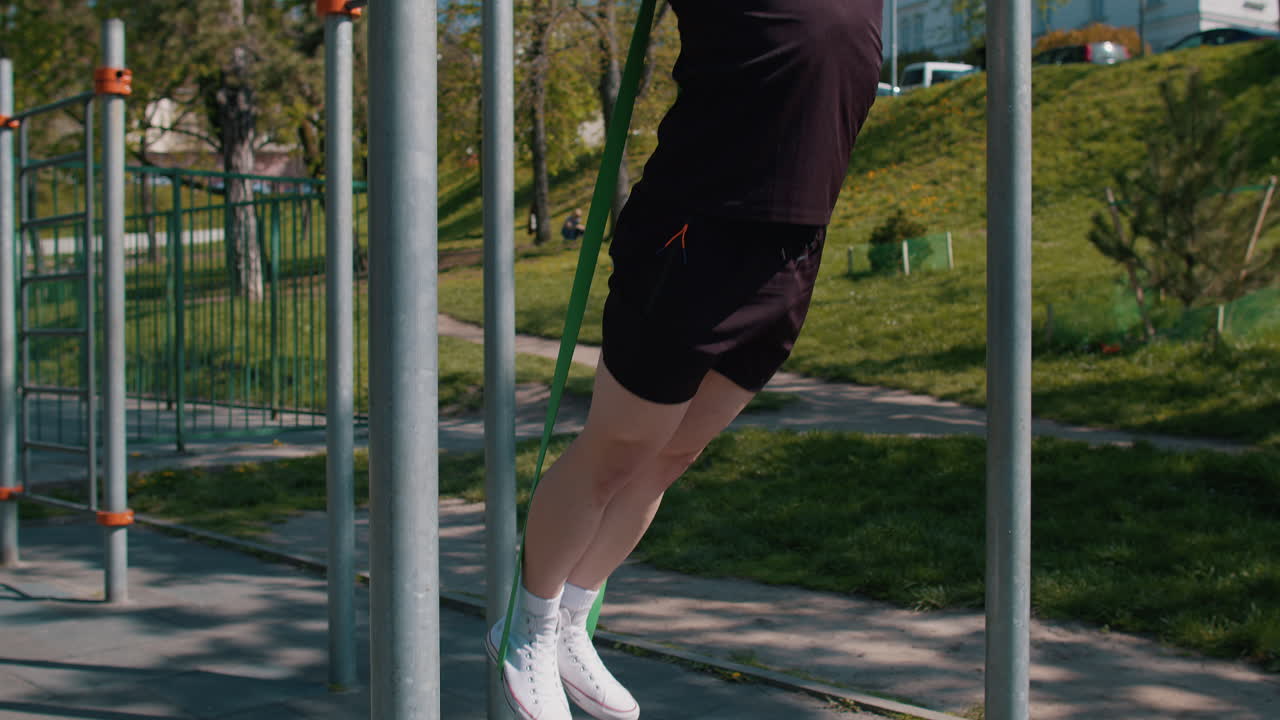 Athletic man in sportswear doing pullups exercises on horizontal bar with help of elastic expander