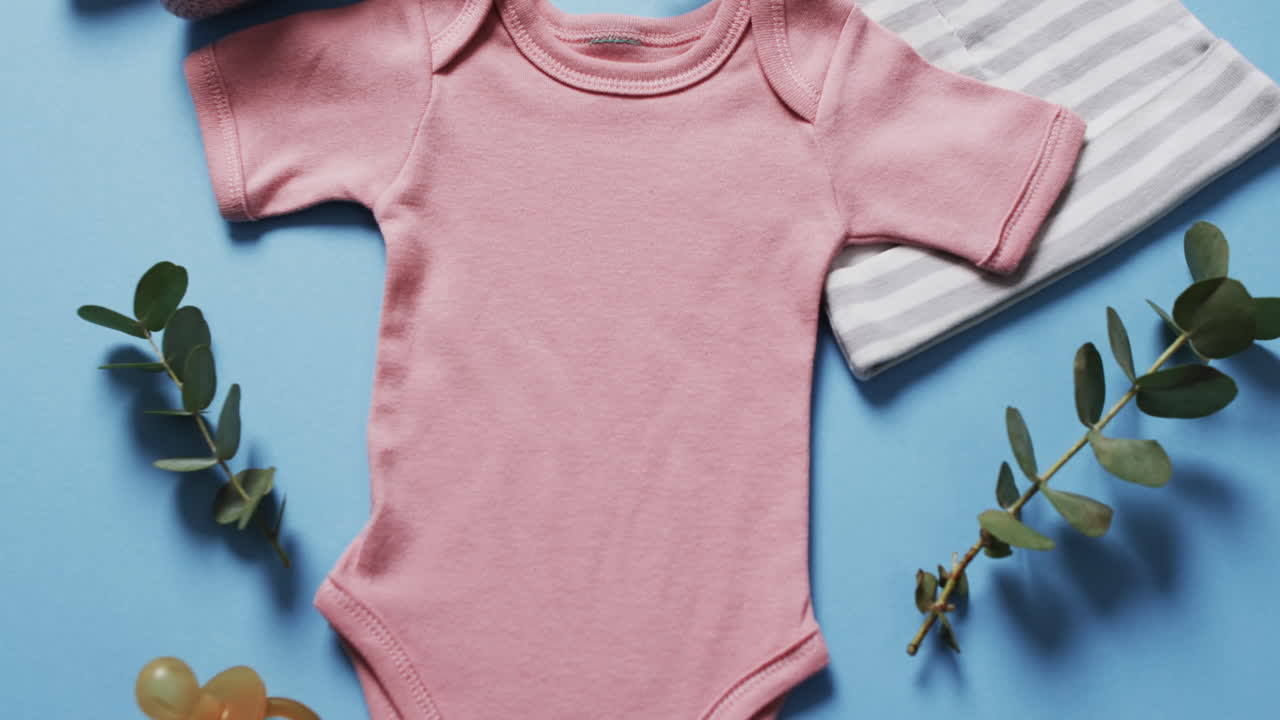 Video of pink baby grow, booties and hat with copy space on blue background