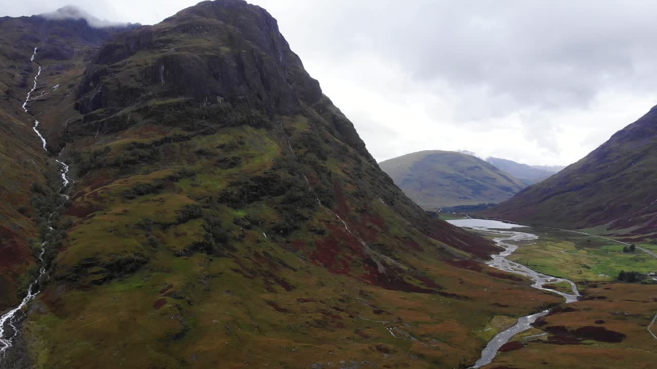 dramática toma aérea al revés de las montañas de glencoe escocia mostrando un río que fluye por la ladera de la montaña