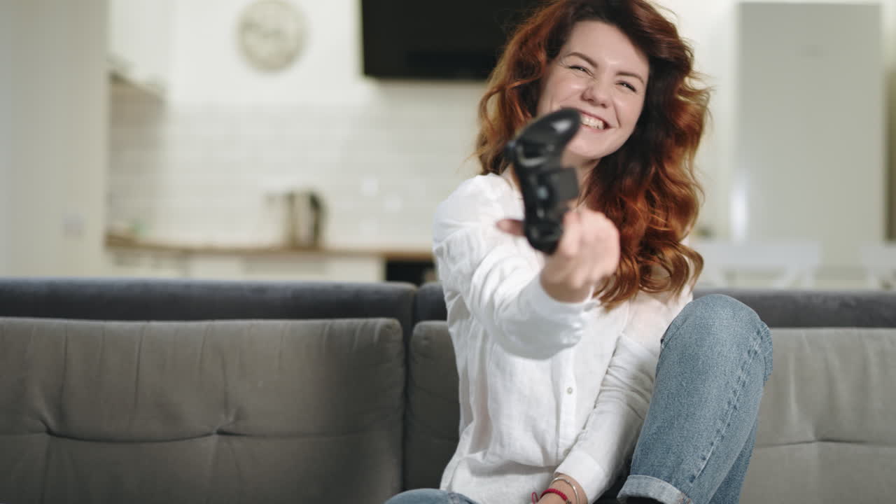 Smilende kvinde spiller videospil i køkkenet. Portræt af en begejstret kvindelig gamer.