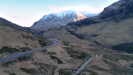 glencoe con montañas cubiertas de nieve y carretera sinuosa al anochecer, paisaje sereno de las tierras altas, vista aérea