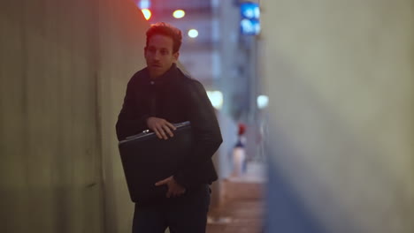 man holding briefcase running away in dark city urban alleyway looking scared. worried and suspicious male with leather jacket. narrow path he runs for police or authority or thief. spy escaping