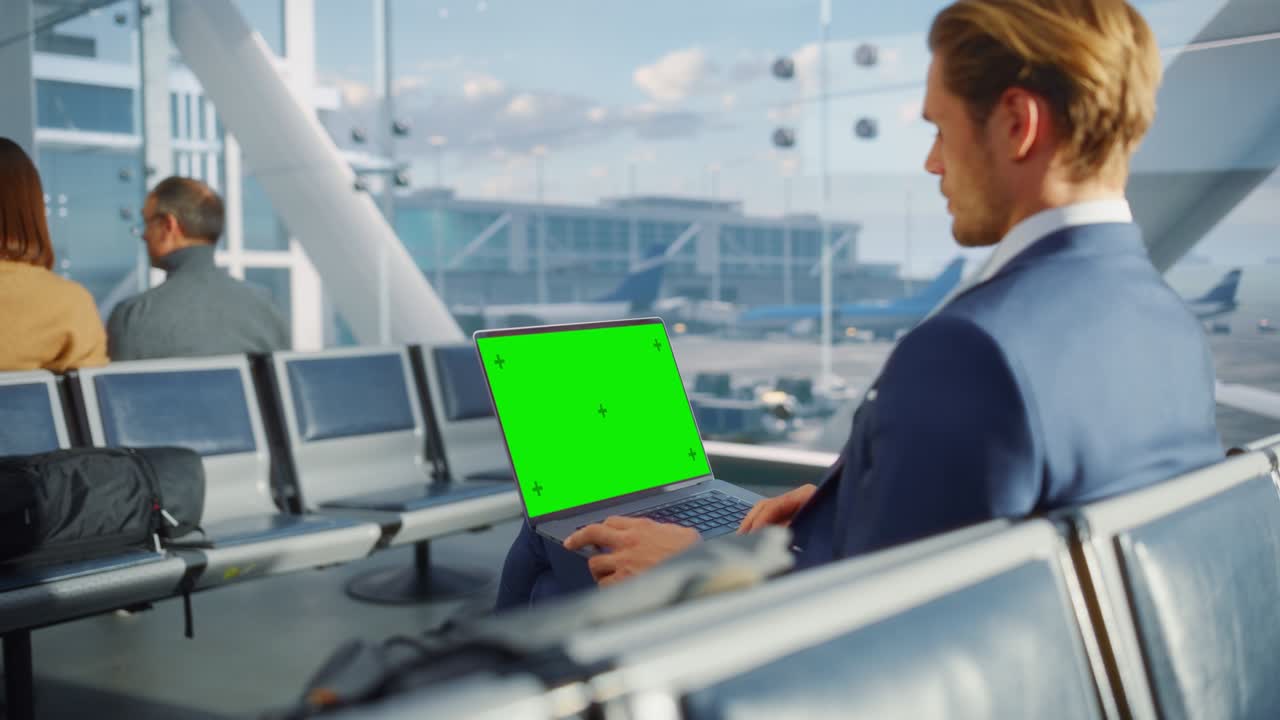 공항 터미널: 비행기를 기다리는 동안 녹색 크로마 키 스크린 노트북에서 일하는 사업가, 항공사 허브의 탑승 라운지에서 온라인 원격 작업을 하는 기업가