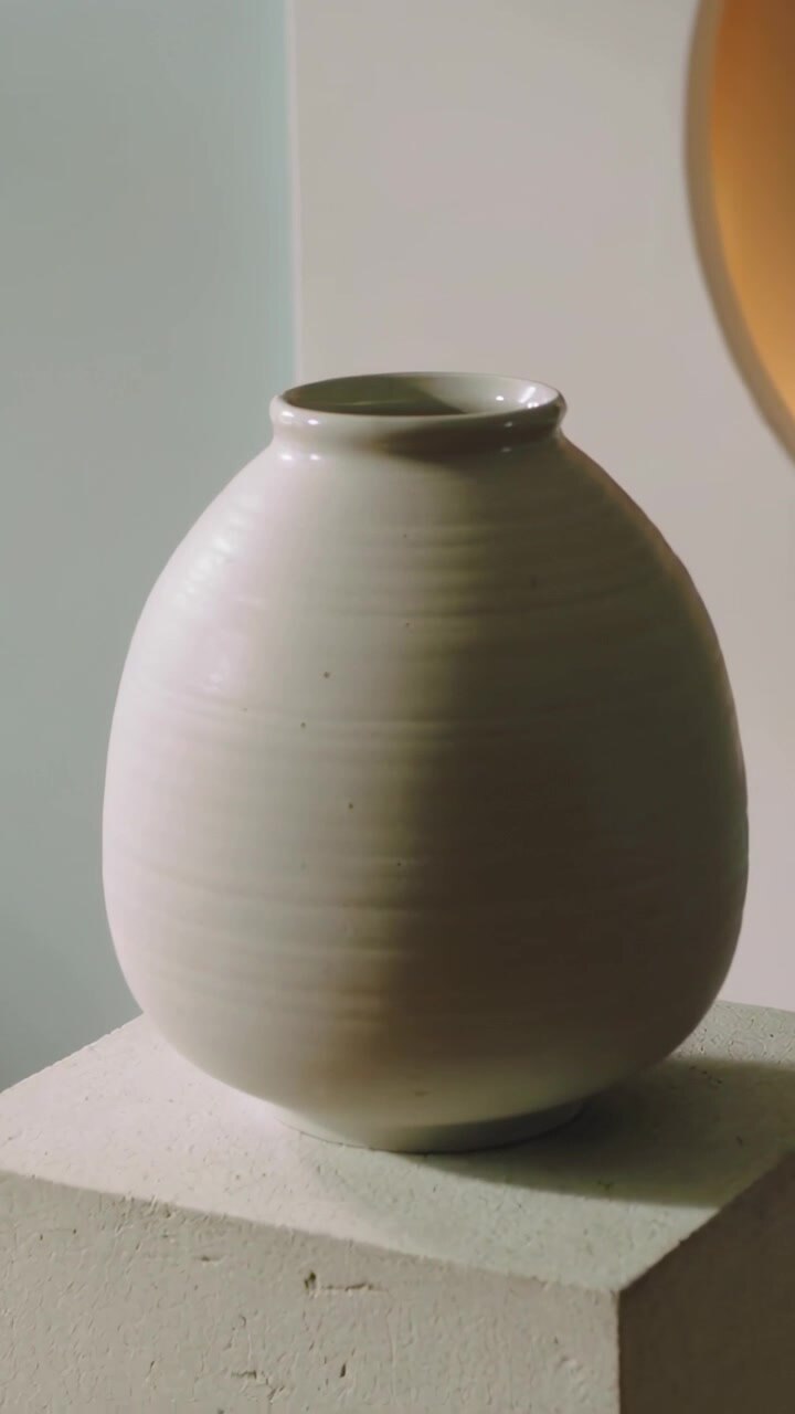 Vertical video: Moving camera panning cream vase on square pedestal in studio revealing niche glow