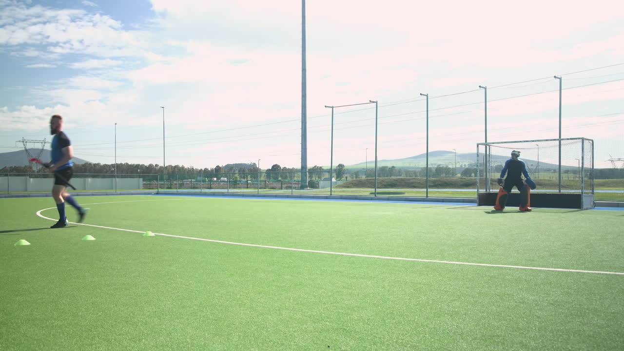 Playing field hockey, man running towards goal with goalkeeper ready to defend