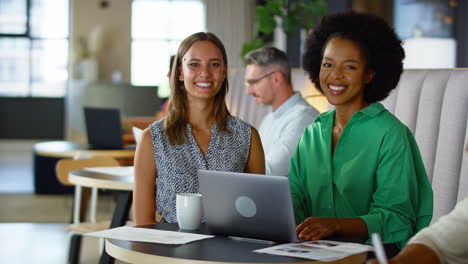 Portrait-Of-Two-Businesswomen-Working-On-Laptop-In-Informal-Seating-Area-Of-Modern-Office