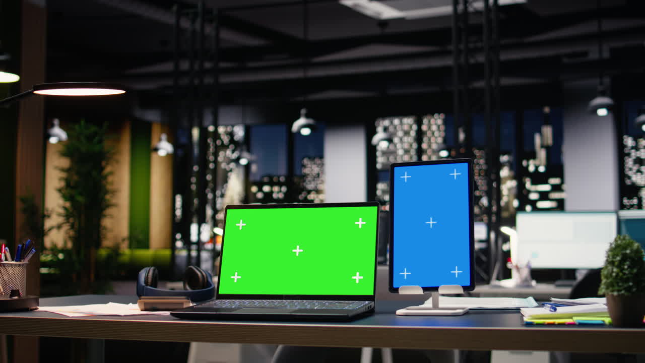 Laptop layar hijau dan layar biru vertikal di interior kantor kontemporer.