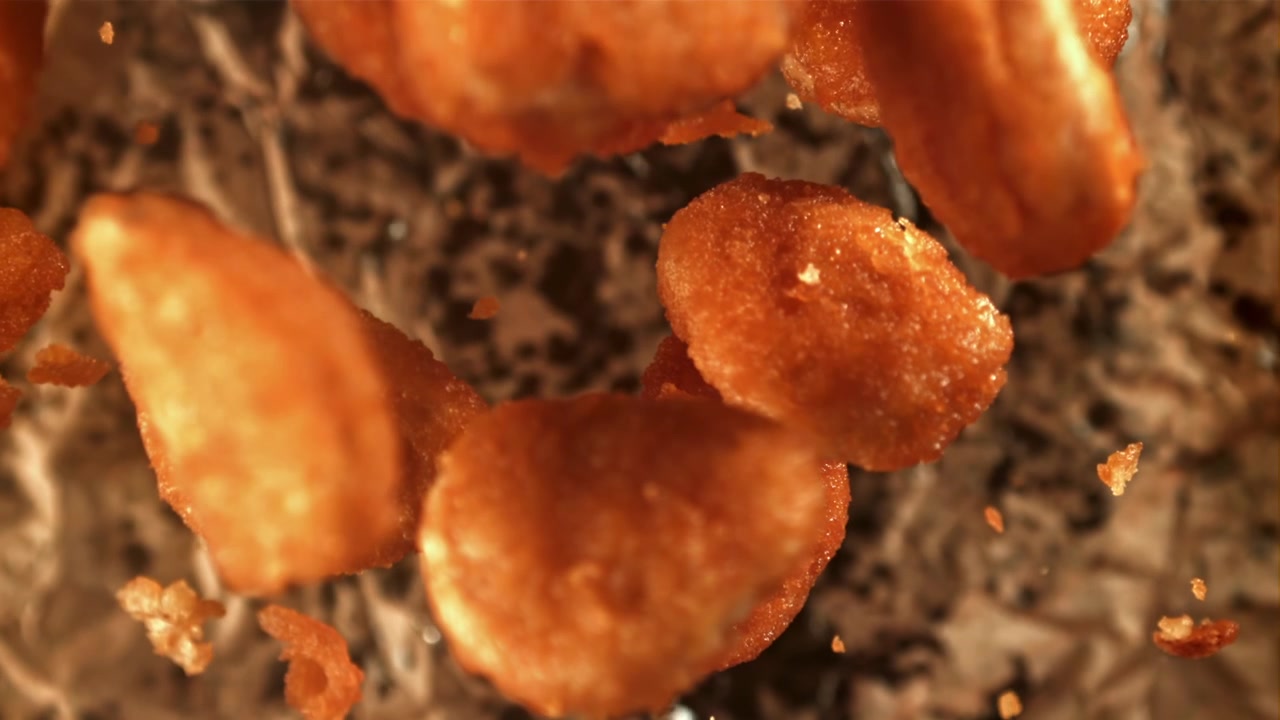 Nuggets de frango fritos e dourados caindo em câmera lenta.