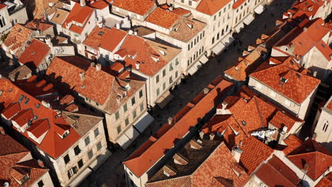 Vista-Aérea-De-Gente-Caminando-En-La-Calle-Entre-Edificios-Típicos-De-Techo-Rojo-En-Dubrovnik,-Croacia