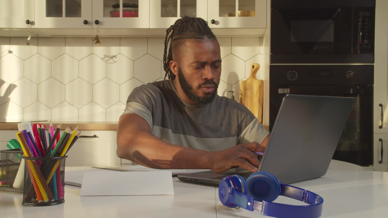 Focused African man with laptop making home accounting routine at home