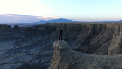 drone circles around man standing on rocky outcropping with stunning utah desert landscape at dawn