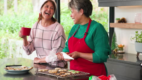 senior women decorating christmas cookies and enjoying hot drinks at home