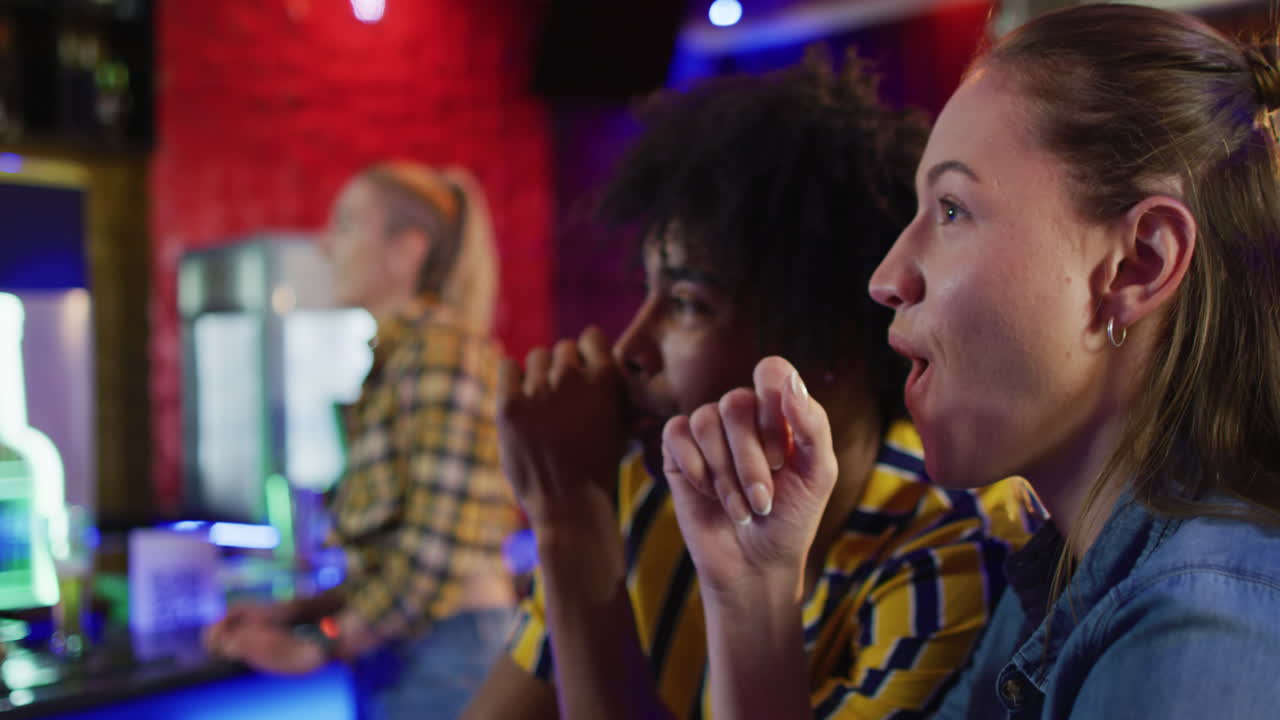 Video di amici uomini e donne di diverse etnie che bevono e reagiscono a una partita sportiva in un bar, festeggiando.