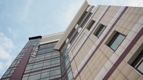 close view of a modern city building with a sleek glass facade and architectural design, the upward perspective highlights the building's structure against a backdrop of a clear blue sky