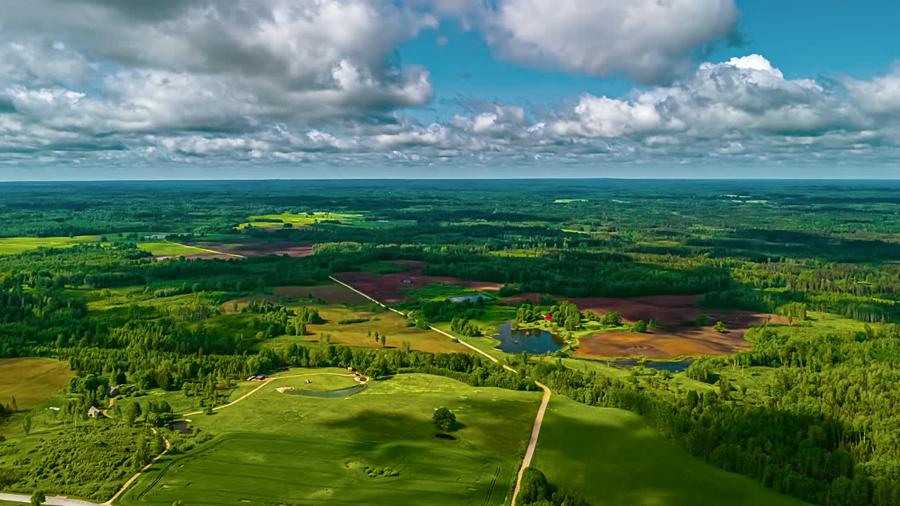 A stunning aerial time-lapse captures fast-moving clouds casting dynamic shadows across a vast and beautiful Latvian landscape of lush green forests, fields, and lakes