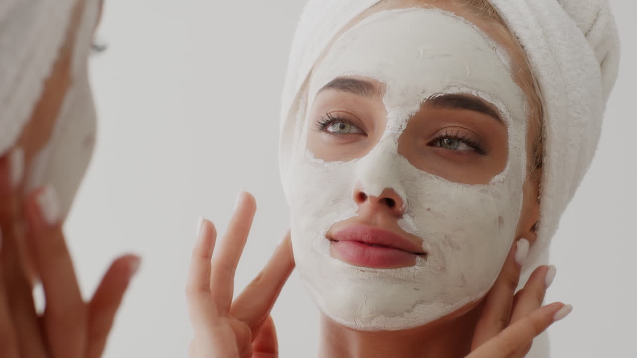 mujer aplicando una máscara facial frente a un espejo