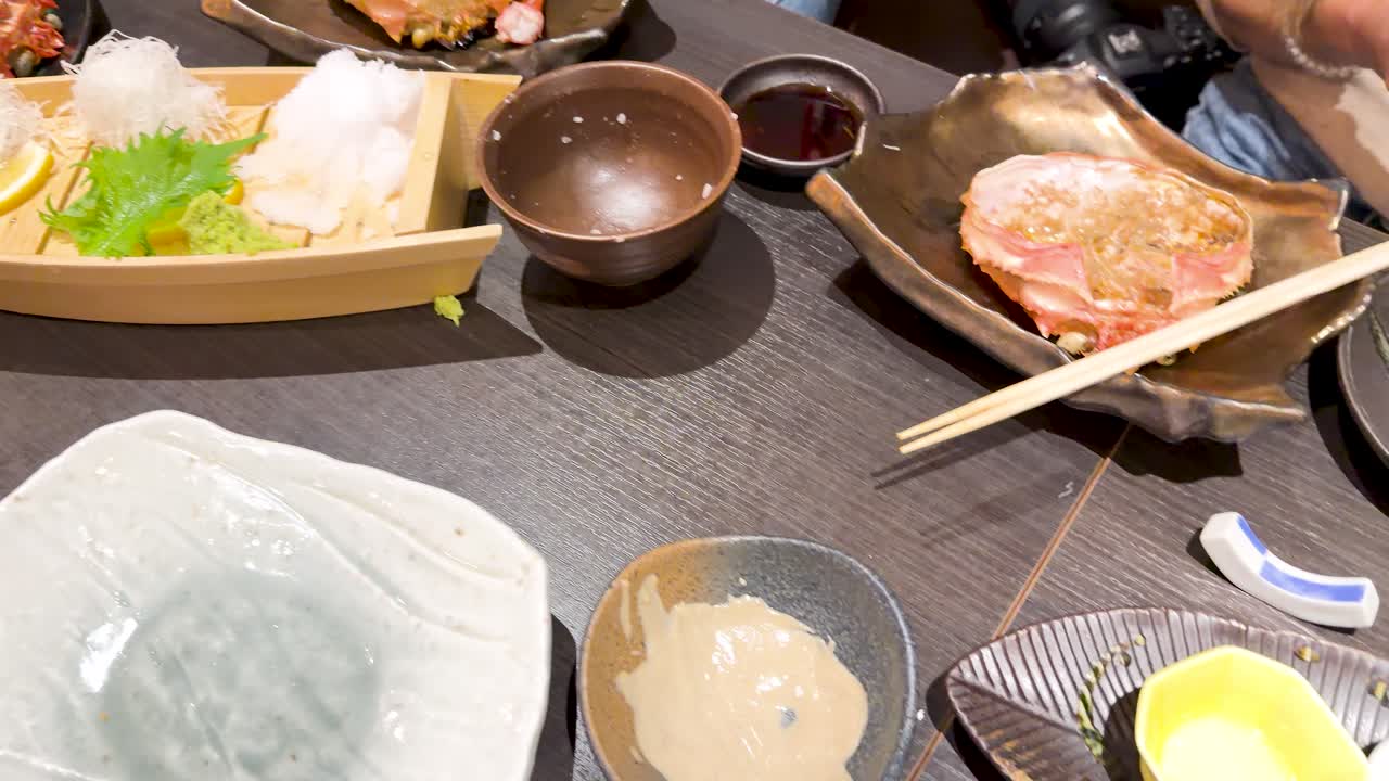レストランのテーブルに並ぶ新鮮な刺身の舟盛りとカニ料理をハイアングルで手持ち撮影したショット。