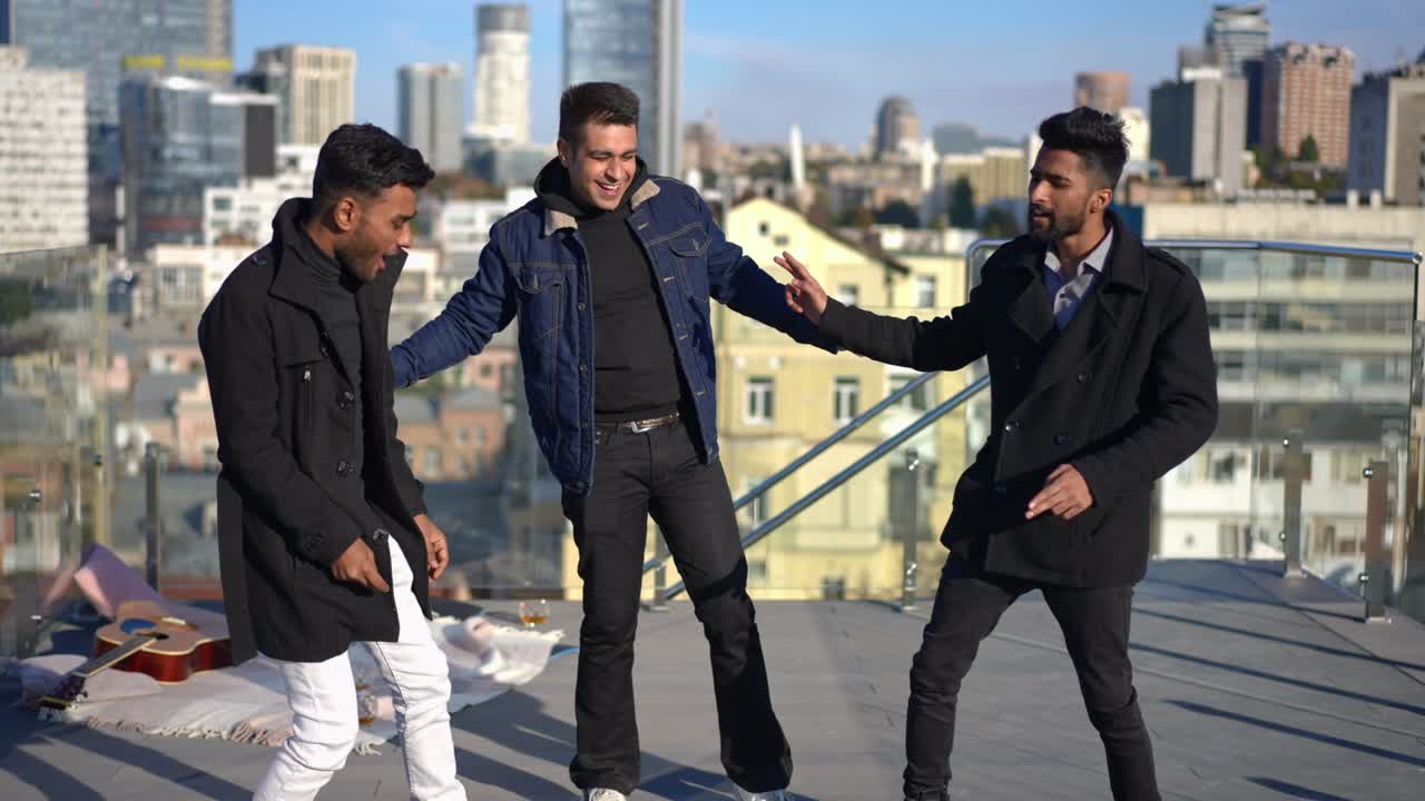 도시에서 은 날 지붕에서 춤을 추는 세 명의 편안한 남성, 긍정적 인 무관심한 중동 남성 친구들이 빛에서 여가를 즐기고, 파티를 축하하는 재미를 즐기고 있습니다.