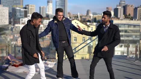wide shot three relaxed men dancing on rooftop on sunny day in urban city. positive carefree middle eastern male friends enjoying leisure in sunshine having fun celebrating partying.