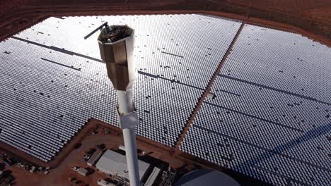 drone shot of a solar thermal energy farm with thousands of mirrors reflecting sunlight onto a central tower where it's converted into heat and used to generate electricity