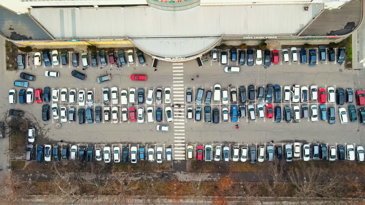 Aerial drone view of Chisinau. View of a parking near a mall, road with moving cars, walking people and bare treest. Moldova