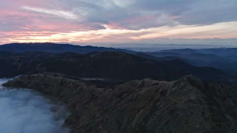 Mountain-peaks-emerging-from-sea-of-clouds-at-dusk,-with-a-serene-sky,-aerial-view