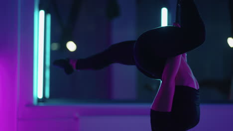 una mujer hace yoga y estiramiento en una hamaca colgante a la luz del neón. una mujer está volando en una hamaca en el estudio haciendo estiramientos y ejercicios corporales. ejercicios en el aire