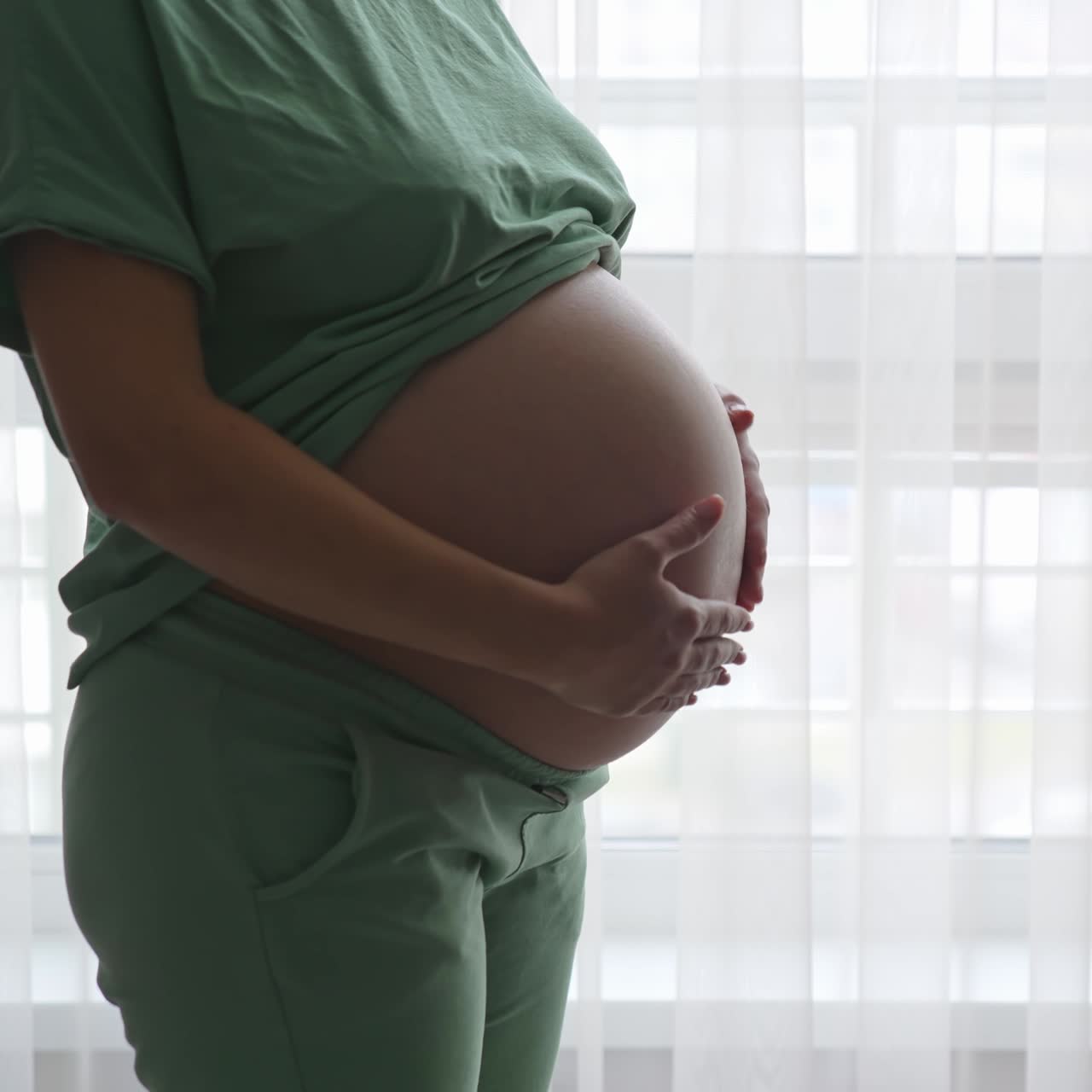 Mujer embarazada de pie cerca de la ventana y relajándose en casa. Concepto de atención prenatal y embarazo