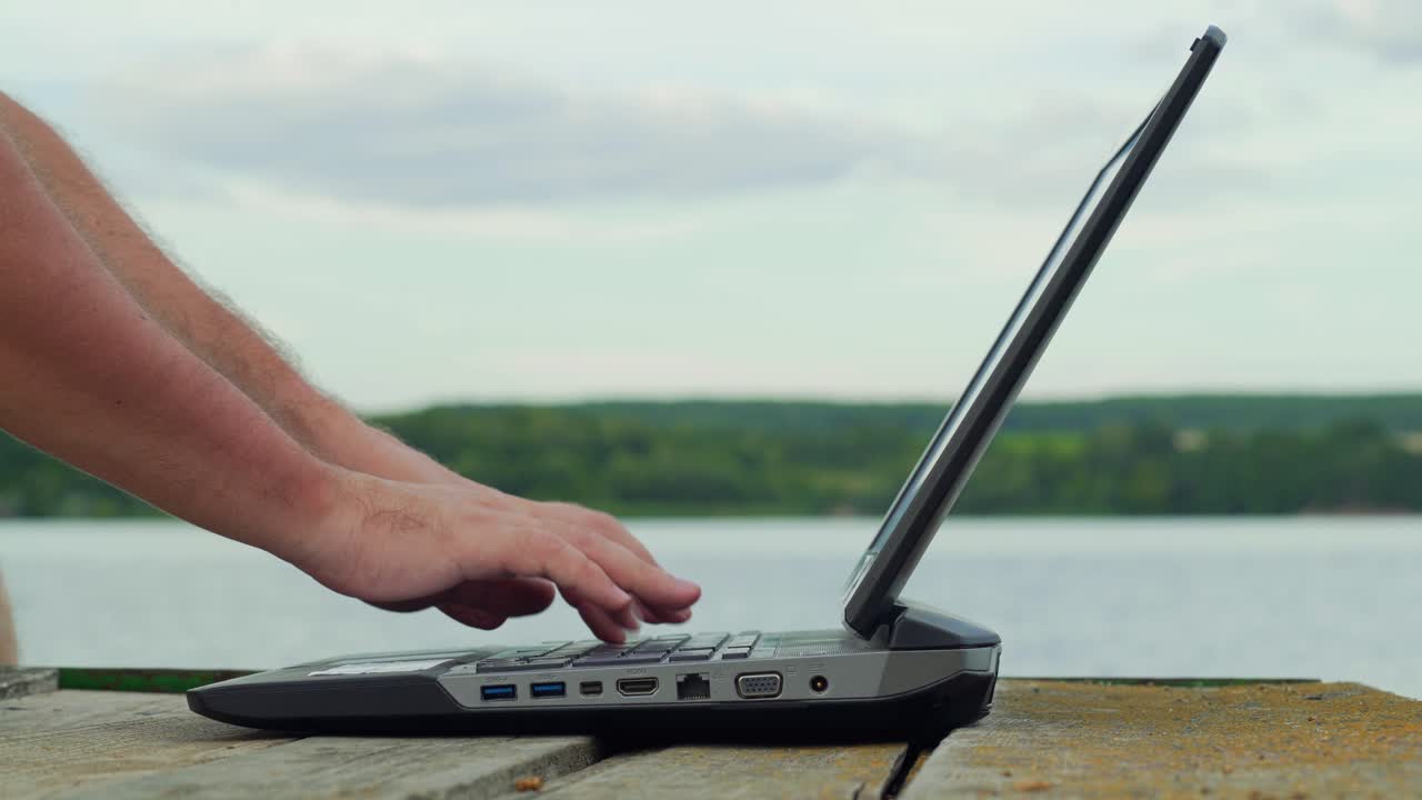 Man's hands using laptop computer. Young man using laptop on the pier.